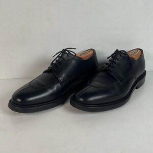 May include: A pair of black leather dress shoes with a rounded toe and lace-up closure. The shoes have a thick sole and are displayed on a white background. Shoe trees are inserted in each shoe.