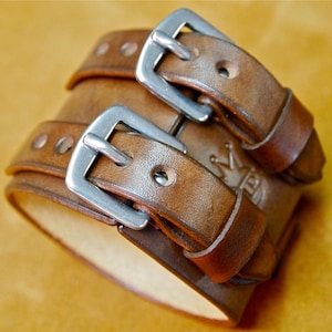 May include: A brown leather bracelet with two silver buckles. The bracelet has a crown and the letter "B" embossed on it.