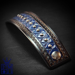 May include: A blue leather bracelet with silver studs and a geometric pattern. The bracelet is curved and has a silver metal accent on the end.