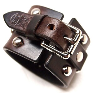 May include: A brown leather cuff bracelet with a silver buckle and studs. The bracelet is double layered and has a distressed look.