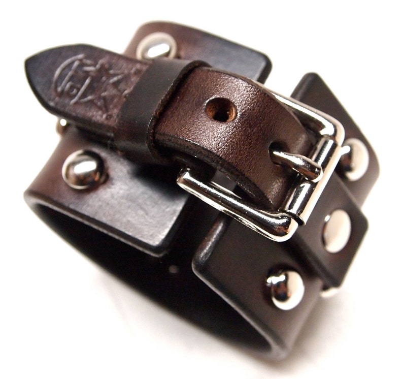 May include: A brown leather cuff bracelet with a silver buckle and studs. The bracelet is double layered and has a distressed look.