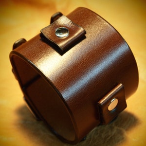 Puede incluir: Una correa de reloj de cuero marrón con dos broches de metal plateado.