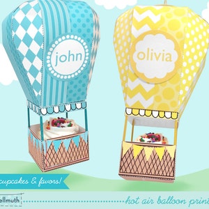 May include: Printable hot air balloon cupcake boxes in blue and yellow with the names "john" and "olivia" printed on them. The boxes are designed to fit mini cupcakes and favors.