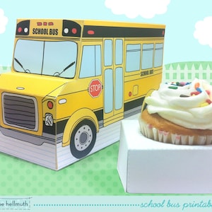 May include: A printable school bus cupcake holder kit. The kit includes a yellow school bus with the words "School Bus" on the front and a cupcake holder. The cupcake holder is white and has a cupcake with white frosting and colorful sprinkles on top.