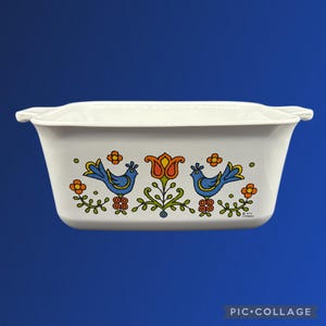 May include: White rectangular casserole dish with a colorful bird and floral design. The design features two blue birds, orange flowers, and a central orange and red tulip. The dish has handles on each end.