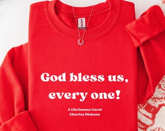May include: A bright red sweatshirt with the quote "God bless us, every one!" in white text. The text "A Christmas Carol, Charles Dickens" is below the quote. A silver necklace with a sunburst pendant hangs from the collar.