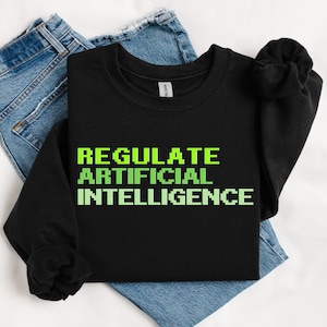 May include: A black crewneck sweatshirt featuring the text REGULATE ARTIFICIAL INTELLIGENCE in a bright lime green pixelated font, paired with a pair of blue denim jeans. The sweatshirt has long sleeves and a ribbed collar, cuffs, and hem.