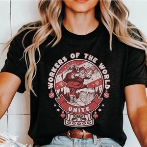 May include: A black t-shirt with a red and white graphic of Santa Claus climbing a chimney. The graphic includes the text "Workers of the World Unite" and "Ho Ho Ho".