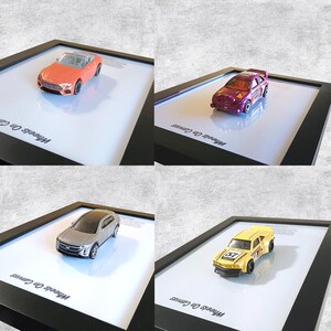 May include: Four framed toy car displays. The cars include a convertible, a hatchback, an SUV, and a race car. The frames are black, and the cars are set on a white background. The text "Wheels On Canvas" is visible on the bottom left of each frame.