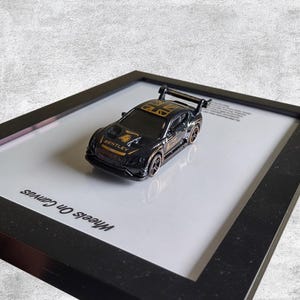 May include: A black and gold Bentley toy car with the number 4 on the hood and a rear spoiler. The car is displayed in a black frame on a white background. The text "Wheels On Canvas" is printed on the frame.