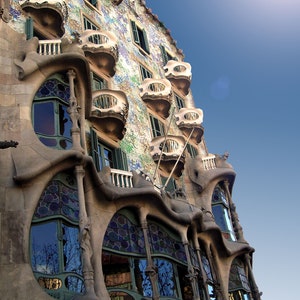 Può includere: Un edificio con un design unico e organico. L'esterno è rivestito di piastrelle a mosaico colorate e presenta numerosi balconi con balaustre in ferro battuto intricate. L'edificio ha un aspetto fantasioso, quasi surreale.