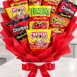 May include: A bouquet arrangement of various snack bags including Flamin' Hot Funyuns, Crunchy Flamin' Hot Cheetos, Chester's Fries, and Flamin' Hot Doritos, wrapped in red tissue paper and placed in a white box with a red ribbon bow.