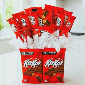 May include: A bouquet arrangement constructed from multiple red KitKat candy bar packages. Two large XL 10 pieces to share KitKat bars form the base, while various smaller KitKat bars are fanned out above, interspersed with white tissue paper.