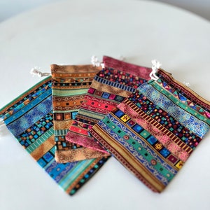 May include: Five small drawstring bags with colorful geometric patterns. The bags are made of fabric and have a variety of colors, including red, blue, green, and gold.