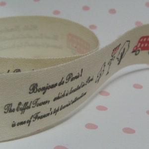 May include: Cream-coloured ribbon featuring red and black illustrations of the Eiffel Tower, a double-decker bus, and other Parisian and London imagery. Text includes "Bonjour de Paris!" and "Hello, the red bus..."