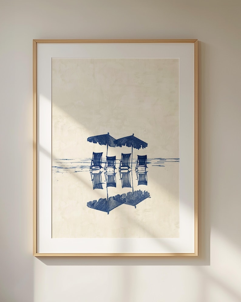 May include: A framed print of a beach scene with four blue chairs and umbrellas reflected in the water. The print is on a beige background.