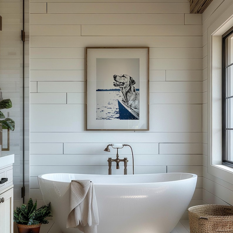 May include: A white freestanding bathtub with a brown towel draped over the edge. The bathtub is in a bathroom with white shiplap walls, a framed print of a dog in a boat, and a window with a view of the outdoors.