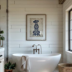 K&ouml;nnte beinhalten: Eine wei&szlig;e freistehende Badewanne mit einem wei&szlig;en Handtuch &uuml;ber dem Rand. Die Badewanne befindet sich in einem Badezimmer mit wei&szlig;en Schiffslappenw&auml;nden und einem gerahmten Druck eines blauen und wei&szlig;en Hundesilhouetten.