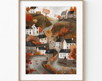May include: A framed art print showing a village scene in autumn. The illustration features houses with dark roofs, a winding road, and trees with orange and red leaves. The artwork is set against a neutral background, with a wooden frame.