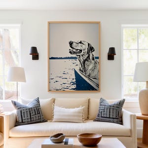 May include: A framed print of a dog in a boat on a lake. The dog is a light brown labrador retriever with its head sticking out of the boat. The water is blue and the sky is white. The frame is a light wood color.