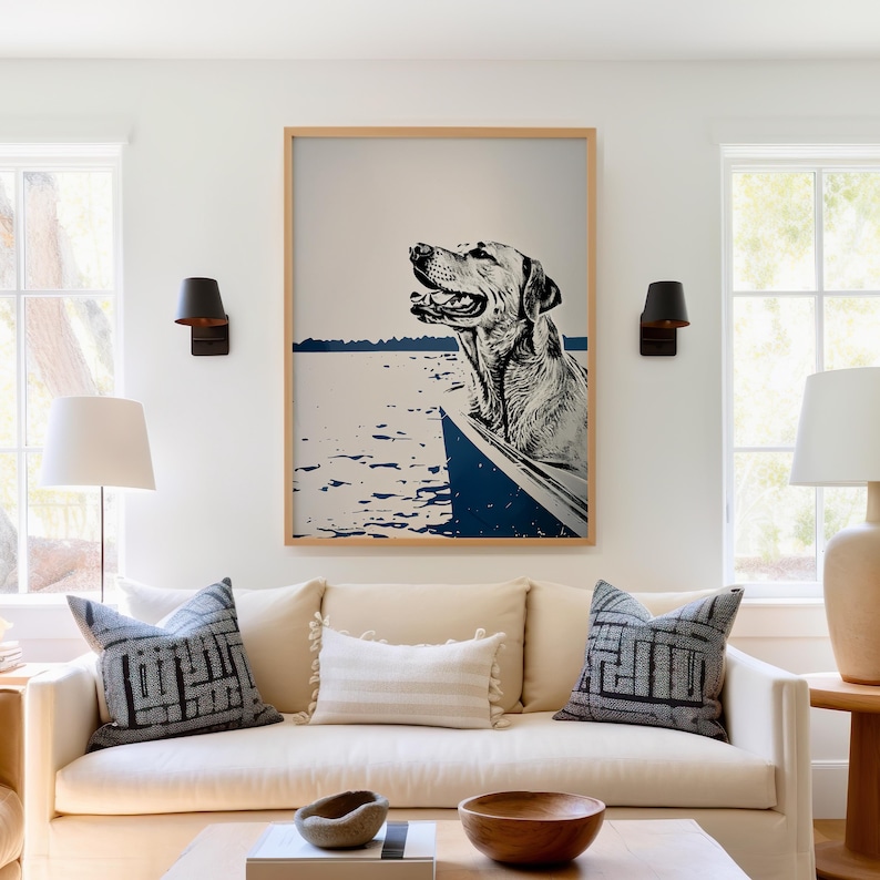 May include: A framed print of a dog in a boat on a lake. The dog is a light brown labrador retriever with its head sticking out of the boat. The water is blue and the sky is white. The frame is a light wood color.
