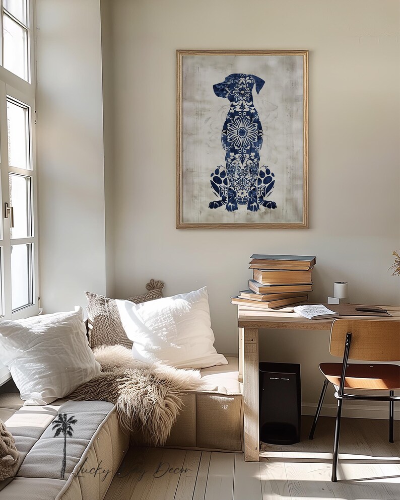 K&ouml;nnte beinhalten: Ein blauer und wei&szlig;er Wandkunstdruck mit einer Hundesilhouette in einem goldenen Rahmen, der an einer wei&szlig;en Wand &uuml;ber einem Holztisch mit B&uuml;chern und einem Stuhl h&auml;ngt.