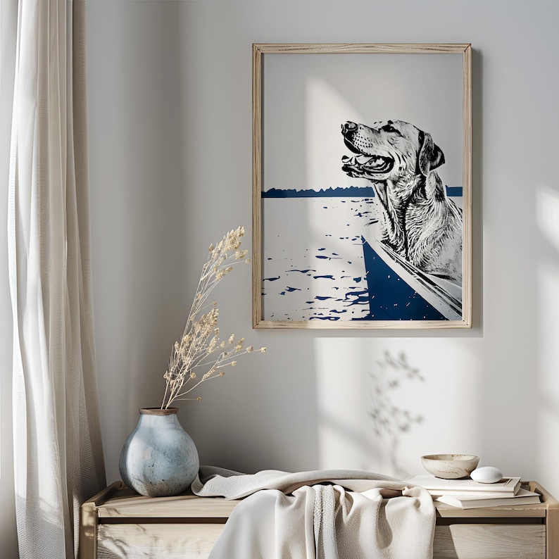 May include: A black and white illustration of a dog in a boat on a blue and white lake. The dog is looking to the right and has its mouth open. The illustration is framed in a light wood frame.