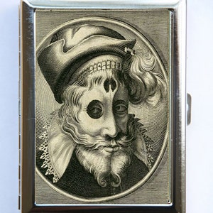 May include: A silver metal cigarette case featuring a detailed black and white engraving of a man in a hat and ruff collar. The portrait is set within an oval frame, creating a vintage aesthetic.