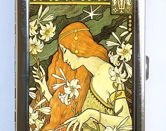 May include: A vintage-style metal cigarette case with a colorful image of a woman with long red hair surrounded by white flowers. The image is set against a green and gold background.