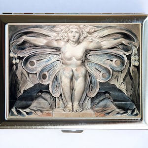 May include: A silver metal cigarette case with a black and white image of a woman with butterfly wings. The woman is sitting on a throne with her wings spread out behind her.