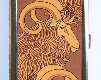 May include: A silver metal cigarette case with a brown and gold illustration of a stylized ram with curly horns and a long, flowing mane.