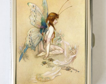 May include: A vintage illustration of a fairy with large butterfly wings. The fairy is kneeling on the ground with a long, flowing dress. The fairy is surrounded by smaller fairies and flowers.