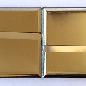 May include: A silver cigarette case with a hinged lid. The case is closed and has a shiny, reflective surface.