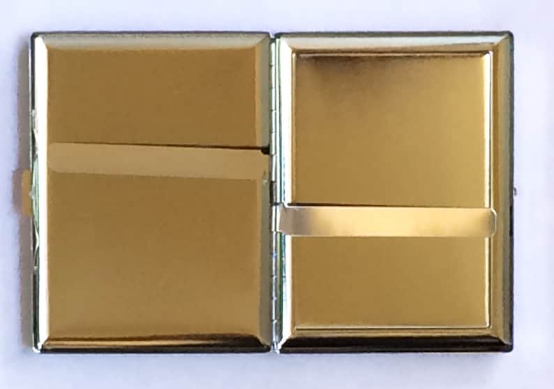 May include: A silver cigarette case with a hinged lid. The case is closed and has a shiny, reflective surface.