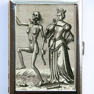 May include: A black and white vintage illustration of a skeleton figure dancing with a woman in a long dress and crown. The image is printed on a silver metal cigarette case.