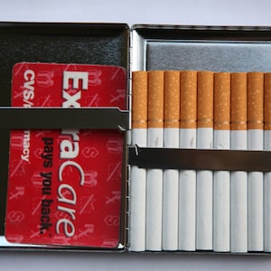 May include: A silver cigarette case with a red ExtraCare card inside and a row of cigarettes in the other side.