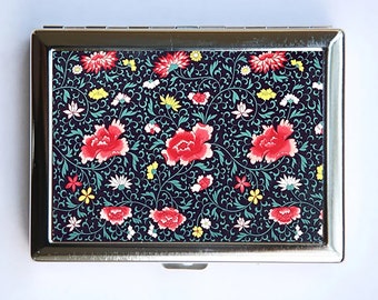 May include: A silver cigarette case with a floral design. The design features red, pink, yellow, and white flowers on a dark blue background.