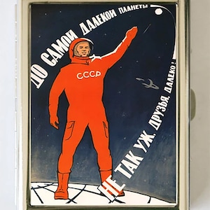 May include: A vintage Soviet propaganda poster featuring an astronaut in an orange spacesuit standing on a planet with the text "To the most distant planet, friends, it's not so far!" in Russian.