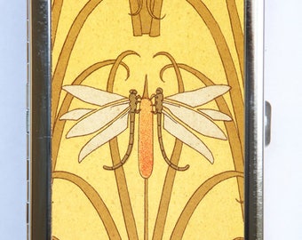 May include: A silver metal cigarette case with a yellow background and a stylized dragonfly design. The dragonfly is white with orange accents.