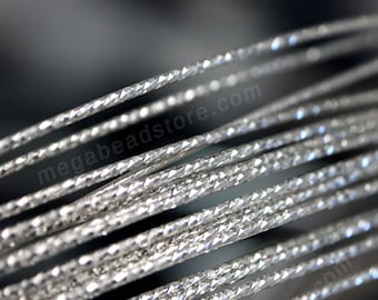 Może przedstawiać: Zbliżenie srebrnego, plecionego drutu z diamentowym wzorem. Drut jest zwinięty i ma błyszczące, metaliczne wykończenie.