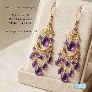 May include: Gold-toned chandelier earrings with teardrop-shaped purple gemstones and smaller purple beads. The earrings have a filigree design and are displayed on a neutral-colored surface. Text on the image reads "Inspiration Example" and "Made with Our Ear Wires Style: F421GF".