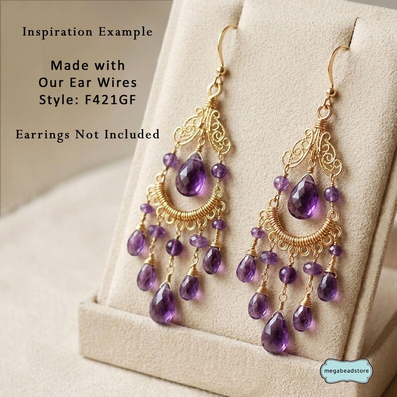 May include: Gold-toned chandelier earrings with teardrop-shaped purple gemstones and smaller purple beads. The earrings have a filigree design and are displayed on a neutral-colored surface. Text on the image reads "Inspiration Example" and "Made with Our Ear Wires Style: F421GF".