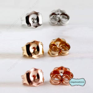 May include: An assortment of earring backs in silver, gold, and rose gold tones. The backs are butterfly style, with a post insertion hole and a curved, secure design. The image includes the text "megabeadstore.com".