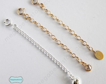 Puede incluir: Tres extensores de cadena de oro y plata con diferentes dijes. El extensor de plata tiene un dije de corazón, el extensor de oro tiene un dije de cristal transparente y el otro extensor de oro tiene un dije redondo.