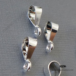 May include: Three silver-toned pendant bails with a loop at the bottom. The bails are designed to be used for attaching pendants to necklaces or bracelets.