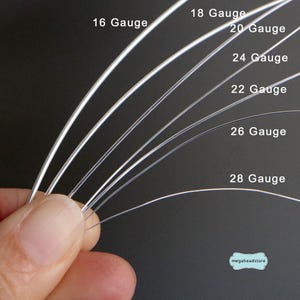 May include: Close-up of several strands of silver-colored wire in varying gauges, from 16 to 28. The wires are curved and held by a hand, showcasing their flexibility. The text "16 Gauge", "18 Gauge", "20 Gauge", "22 Gauge", "24 Gauge", "26 Gauge", and "28 Gauge" is visible.