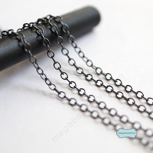 May include: Four strands of black chain, each with a different length, are displayed on a black surface. The chain is made of small, round links.