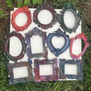 May include: Nine ornate picture frames with iridescent finishes. The frames are in various shapes, including heart, oval, and rectangular. The frames are all different colours, including blue, purple, green, and red.