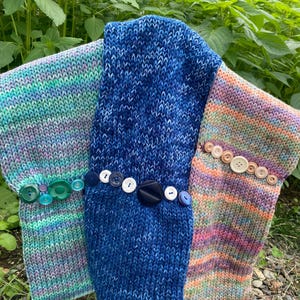May include: Three knitted scarves with different color patterns and buttons. The scarves are blue, green, and pink with white and brown stripes.