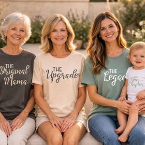 Puede incluir: Cuatro personas con camisetas a juego con los textos: "The Original Mama", "The Upgrade", "The Legacy" y "The New Chapter". El grupo está sentado en un banco al aire libre. Las camisetas son de varios colores, incluyendo gris, beige y verde.